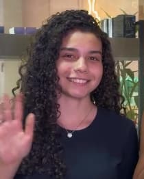 Carine, de cachos longos e definidos, castanho-escuros.